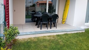 Eine Terrasse mit Tisch und Stühlen, ein gelbes Surfbrett und eine Glastür, die in einen Garten führt.