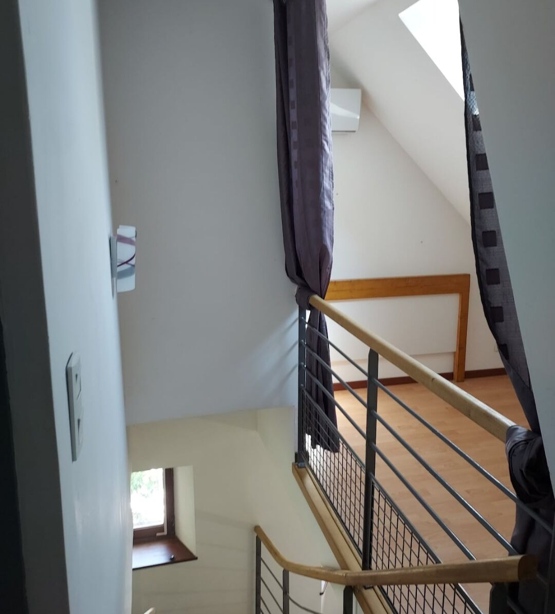 Een trap met een houten leuning en metalen spijbels, leidend naar een kamer met een schuine kap en een raam.