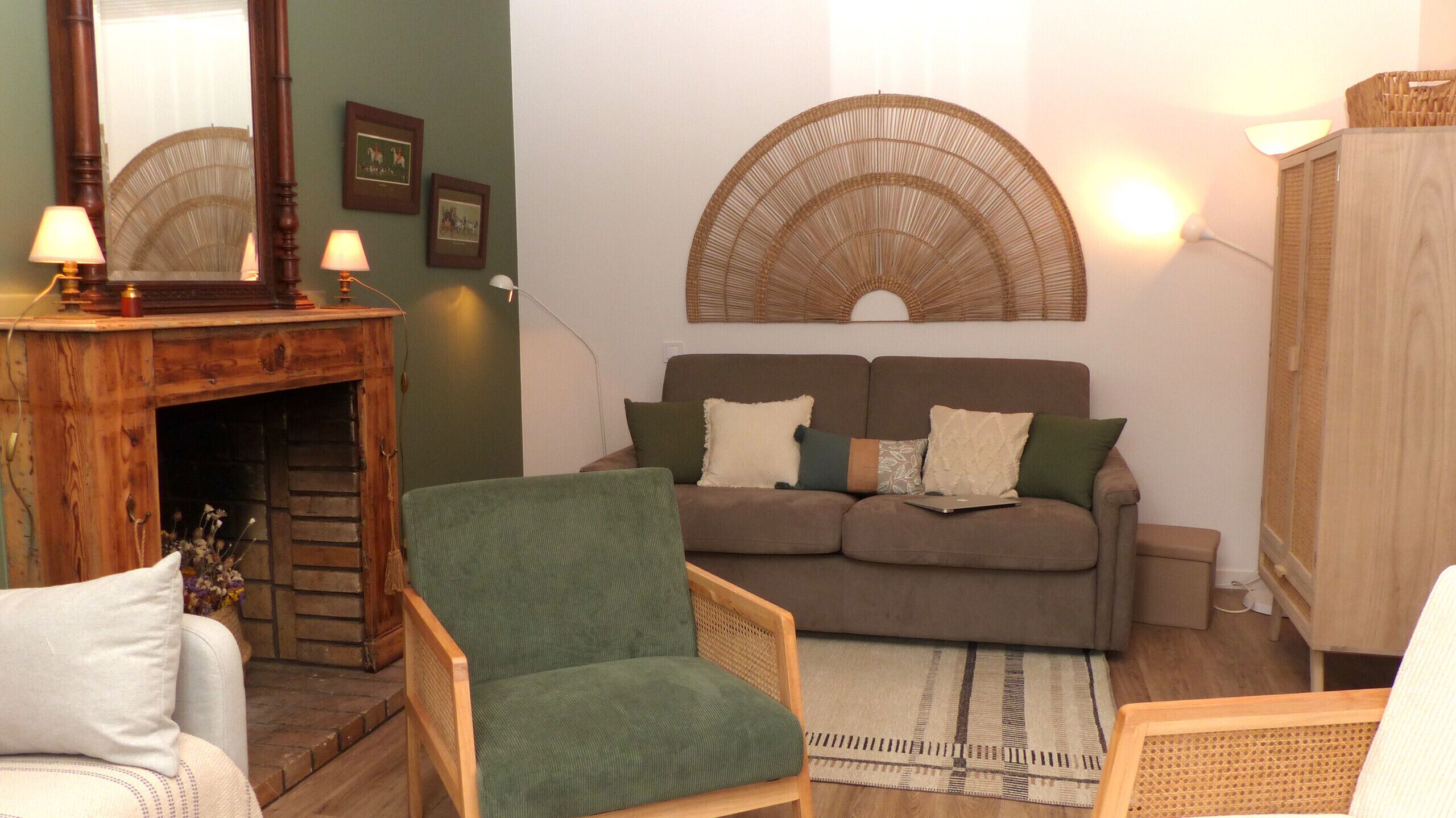 A cozy living room with a fireplace, a green armchair, a sofa with multiple cushions, and a woven wall hanging.