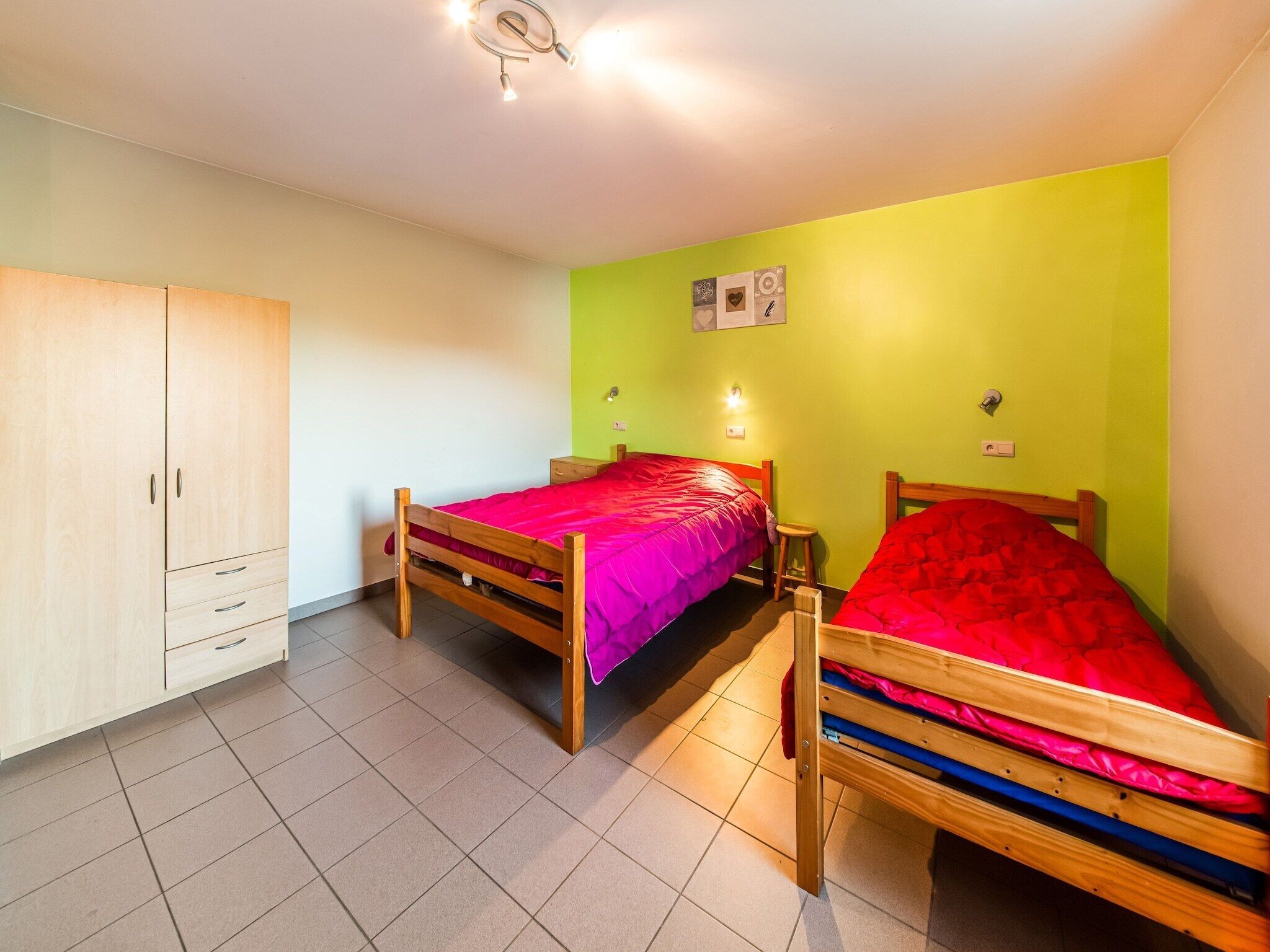 Une chambre avec deux lits en bois, une armoire et un mur vert.
