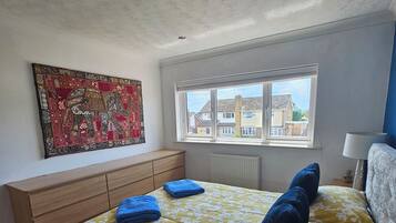 A bedroom with a bed, a window, a radiator, and a wall-mounted artwork.