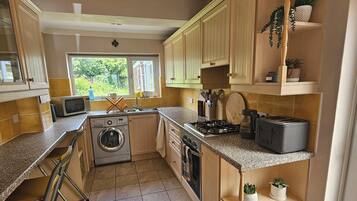A compact kitchen with wooden cabinets, a built-in washing machine, a gas stove, and a toaster.