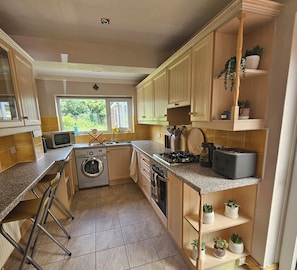 A compact kitchen with wooden cabinets, a built-in washing machine, a gas stove, and a toaster.