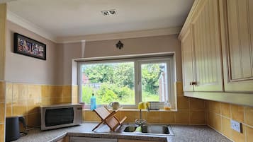 A compact kitchen with a washing machine, microwave, and a window with a view of greenery.