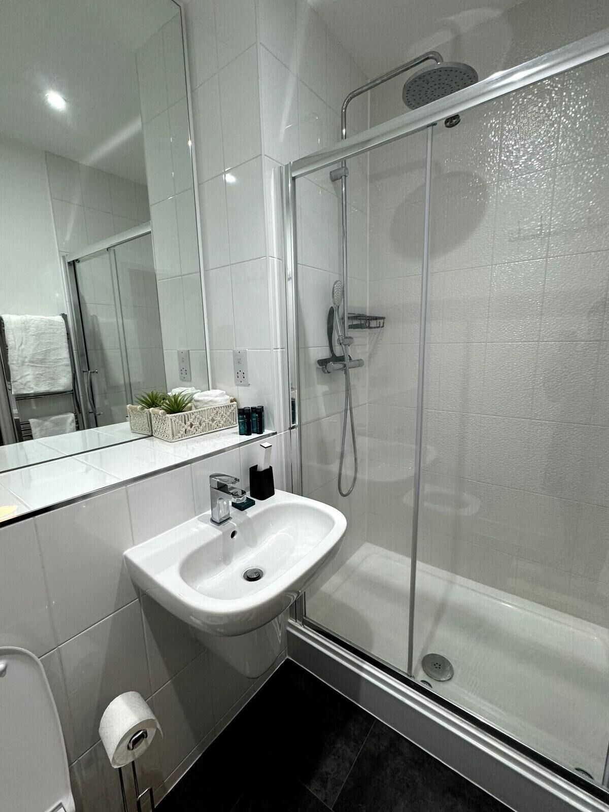 Een moderne badkamer met een douchecabine van glas, een witte wastafel en een grote spiegel.