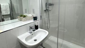Een moderne badkamer met een douchecabine van glas, een witte wastafel en een grote spiegel.