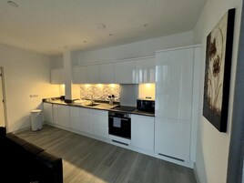 A modern kitchen with white cabinets, a black countertop, and a marble backsplash.