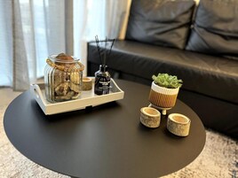 A modern living room with a black coffee table, a glass jar with decorative items, a small potted plant, and a diffuser on the table.