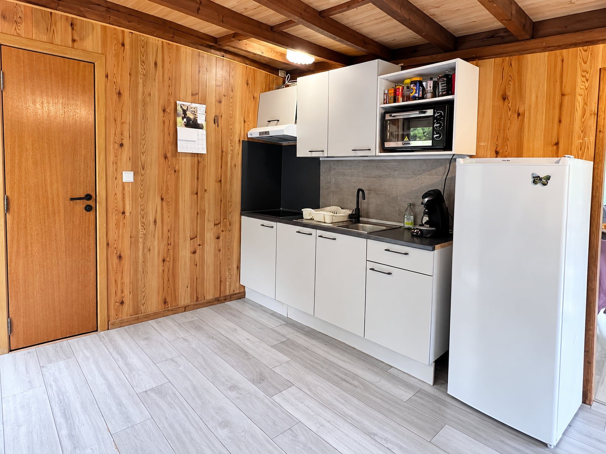Een keuken met houten kastjes, een magnetron, een spoelbak en een koelkast.