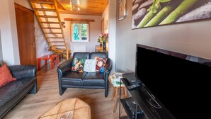 A cozy living room with a black leather sofa, a black armchair, a wooden ladder, a flat-screen TV, and a coffee table. - Cozy Family Cottage in Érezée (Erezée)