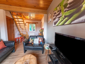 A cozy living room with a black leather sofa, a black armchair, a wooden ladder, a flat-screen TV, and a coffee table. - Cozy Family Cottage in Érezée (Erezée)