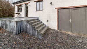 A modern house with a concrete staircase leading to a door, a small patio with a table, and a garage door. - Cozy Family Cottage in Érezée (Erezée)