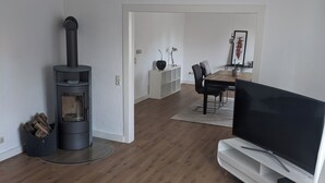 A modern living room with a wood-burning stove, a TV, and a dining area. - Coesfeld outskirts - Quiet apartment for 2 persons, close to town and nature (Coesfeld)