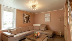 Una sala de estar con un sofá seccional color beige, una mesa de centro de madera con flores y obras de arte en las paredes.