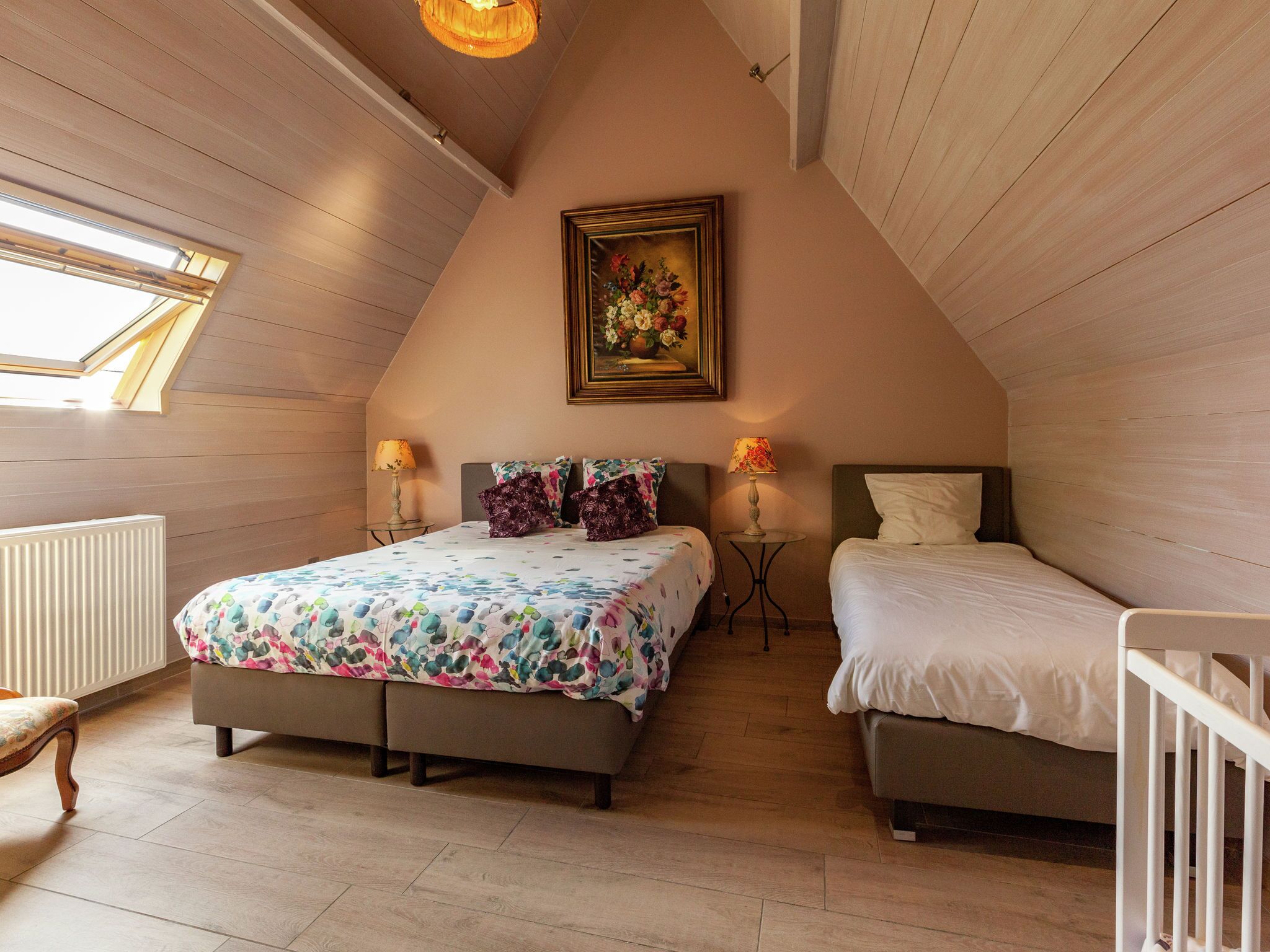 A bedroom with a sloped ceiling, two beds, a radiator, a small table, and a painting on the wall.