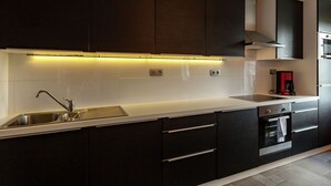 Una cocina moderna con armarios oscuros, un lavamanos de acero inoxidable y un horno empotrado.