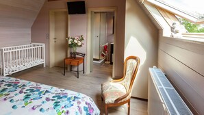 Un dormitorio con techo inclinado, una cuna, una silla, un radiador y una ventana con vistas.