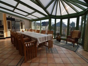 A conservatory with a dining table, chairs, and a kitchen area.