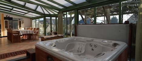 A hot tub in a conservatory with a dining area and a kitchen.
