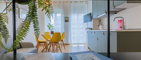 A modern kitchen with a dining area, a TV mounted above the counter, and a potted plant.
