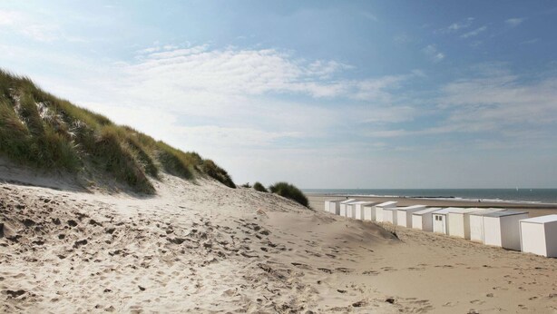 En strand med sanddyner och badhytter i bakgrunden.