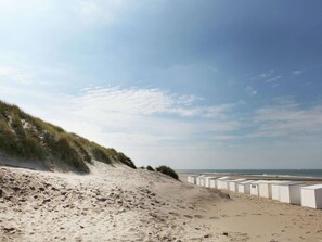 Une plage avec des dunes de sable et des cabanes de plage en arrière-plan.