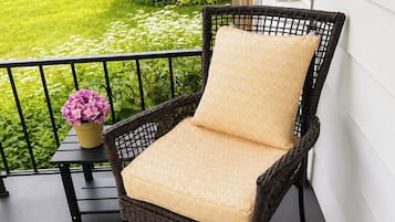 A wicker chair with a cushion on a balcony with a railing.
