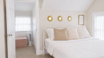 A bedroom with a white bed, a bench, and a radiator. There are three wall decorations and a framed picture.