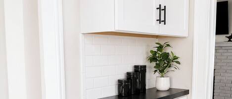 A kitchen with white cabinets, black handles, a black countertop, and a potted plant.
