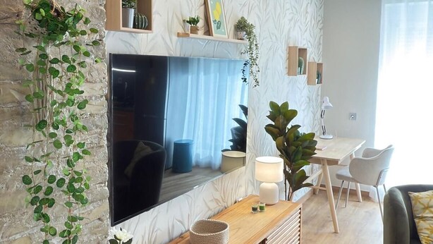A modern living room with a stone accent wall, a large flat-screen TV, a wooden console table, and a dining area with a white table and chairs.