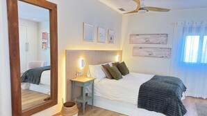 A bedroom with a bed, bedside table, mirror, and ceiling fan.