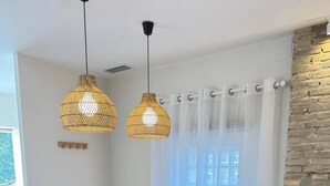 A dining area with a wooden table, four chairs, two hanging wicker pendant lights, and a window with sheer curtains.