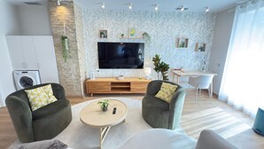 A modern living room with a flat-screen TV, two armchairs, a coffee table, and a desk with a chair.
