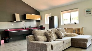 A modern living room with a sectional sofa, a kitchen area with dark cabinetry, and a dining area with a wooden table and chairs. - Exclusivo Loft en Zaragoza-2 (Movera)