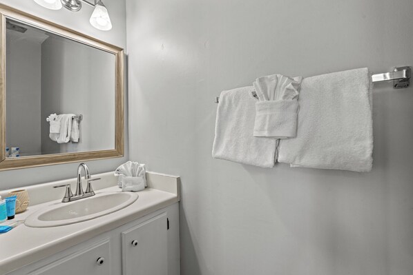 A bathroom with a sink, mirror, and towel rack. - 2-bedroom condo in N. Myrtle Beach offers the peace of the waves within a walk. (North Myrtle Beach)