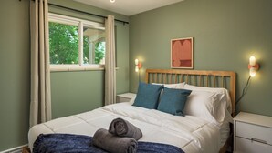 Un lit bien fait, avec du linge de lit blanc et des oreillers bleus, une table de chevet avec une lampe et une fenêtre avec des rideaux.