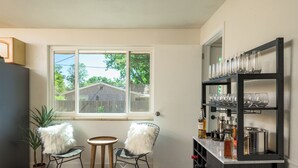 Une cuisine avec une fenêtre, deux chaises, une petite table et un coin bar avec des étagères.