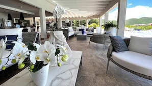 Ein geräumiger Lounge-Bereich mit Deckenventilator, bequemen Sitzgelegenheiten und Blick auf Pool und Berge.