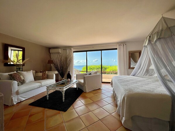 A hotel room with a bed, a sofa, a coffee table, and a view of the ocean.