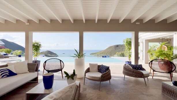 Ein großzügiger Lounge-Bereich mit Blick auf das Meer und die Berge, ausgestattet mit Sofas und Sesseln und begrünt mit Topfpflanzen.