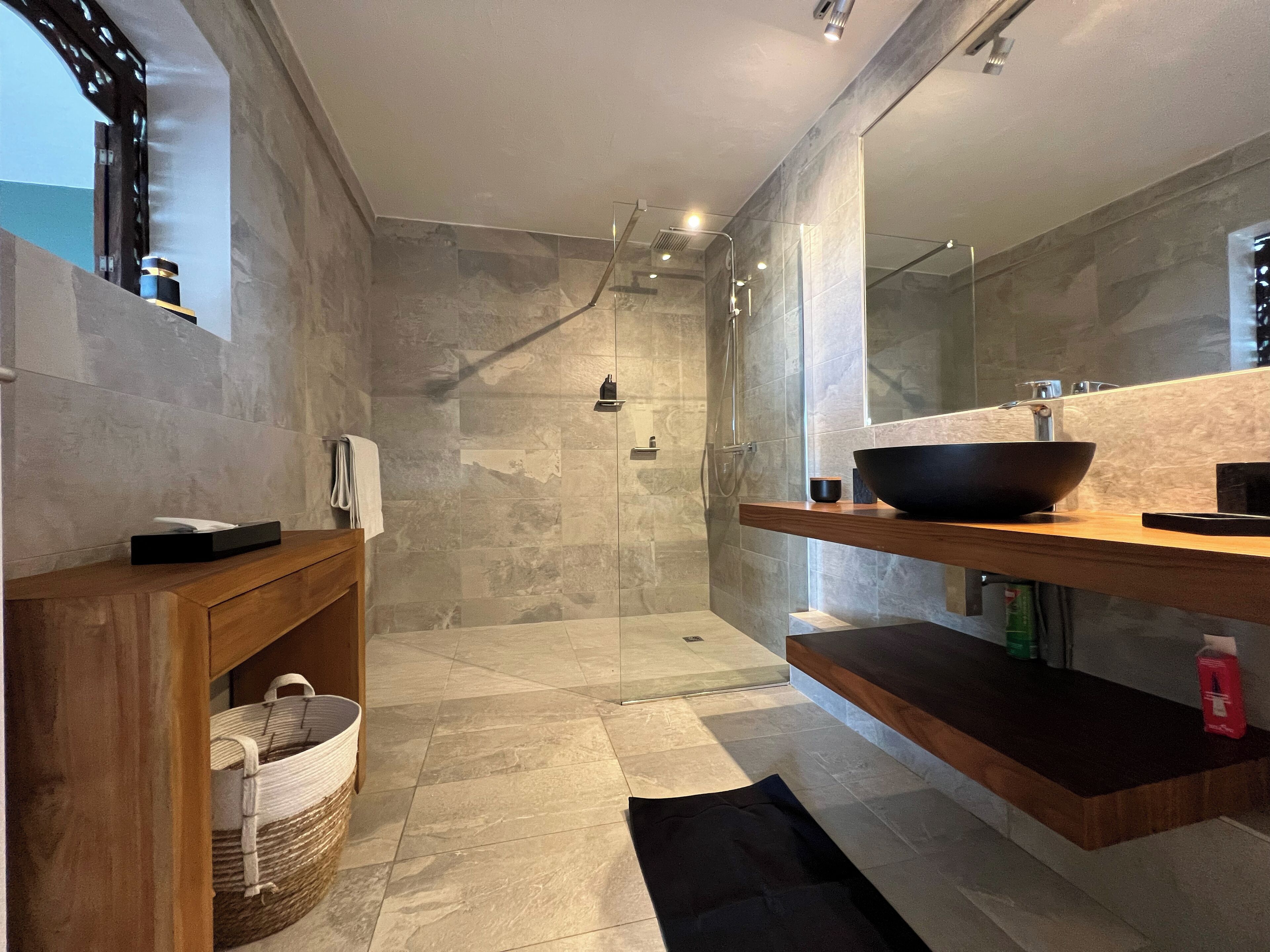 A modern bathroom with a walk-in shower, a wooden vanity, a large mirror, and a black basin.