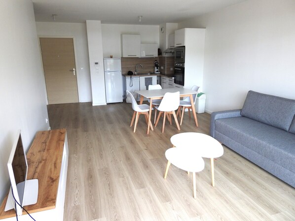 A modern kitchen with white appliances, a dining area with a wooden table and white chairs, and a grey sofa. - T3 Tout Confort à Capbreton - XXL Balcony, Double Parking, Assured Quietness (Capbreton)