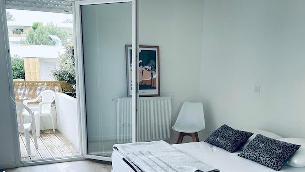 A modern bedroom with a large bed, a radiator, a chair, and a view of the outside balcony.