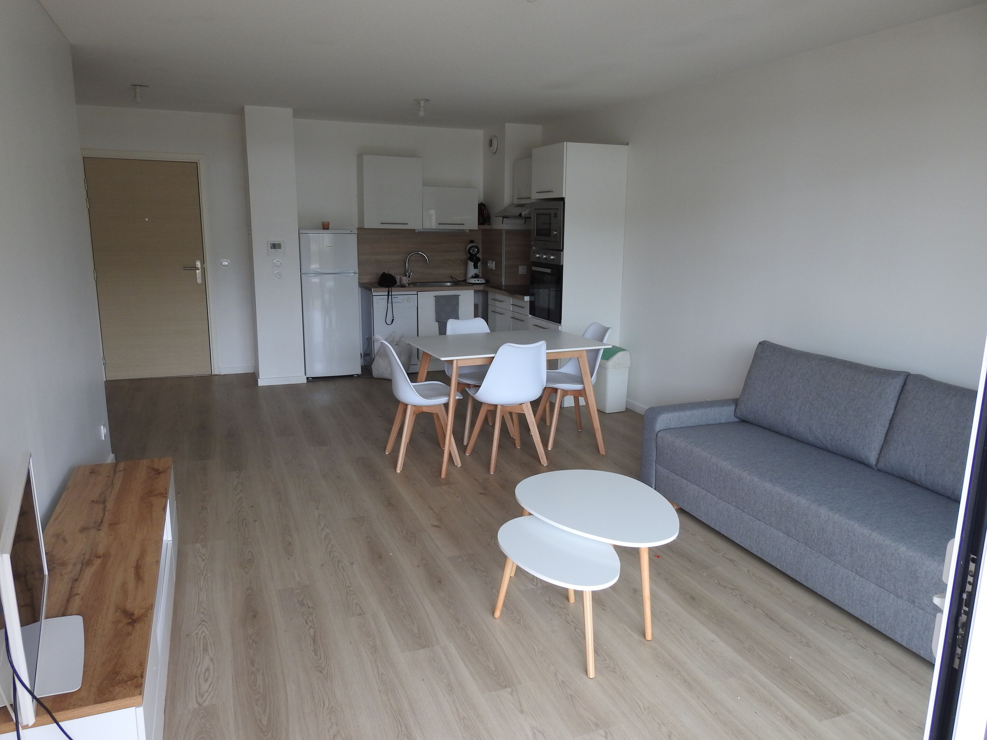 A modern living space with a dining area, kitchenette, and a grey sofa.