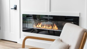 Un intérieur moderne avec une cheminée en verre, une chaise en bois et une porte blanche dotée d’un clavier pour l’ouverture à code.