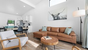 Un salon moderne avec un canapé d’angle, une table basse en bois et un coin repas avec une cuisine en arrière-plan.