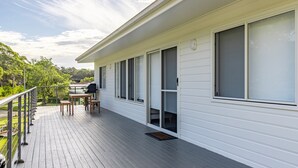 Una terraza techada con una parrilla, asientos al aire libre y vistas a un área boscosa.