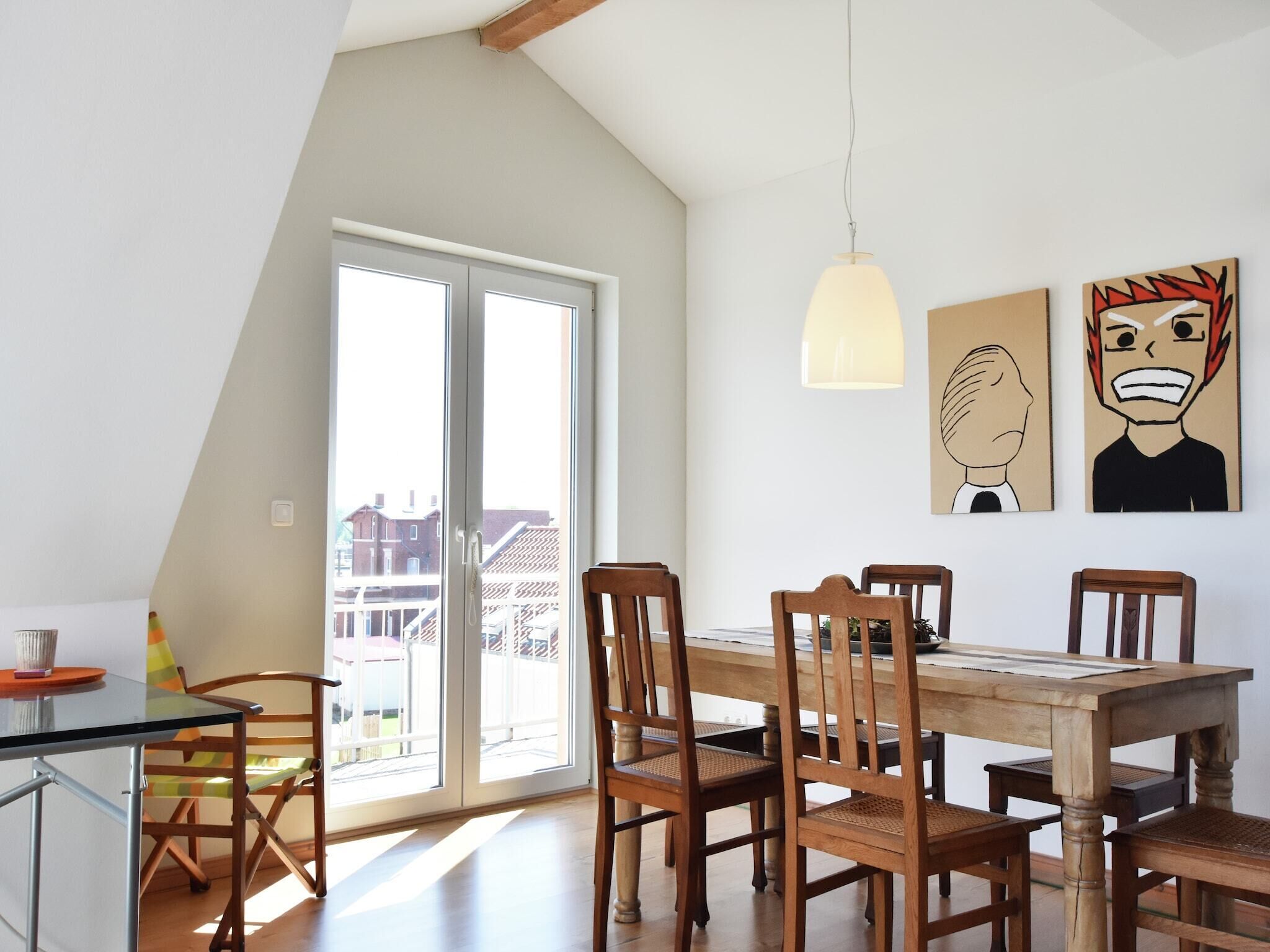 Ein Essbereich mit einem Holztisch und Stühlen, einer hängenden Pendelleuchte und einer Glasschiebetür, die auf einen Balkon im Freien führt.