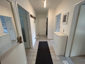 Ein Flur mit einer schwarzen, strukturierten Matte, weißen Wänden, einer weißen Tür und einem weißen Schrank.