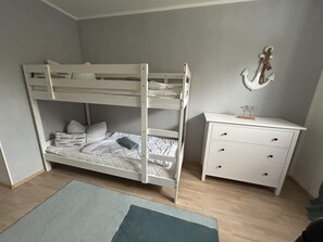 Un lit superposé avec un bureau et des tiroirs, un petit tapis et un élément décoratif en forme d’ancre fixé au mur.